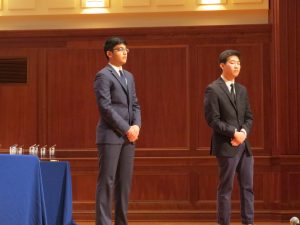 Two people standing up on stage presenting their mayo business plan