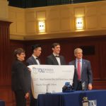 Four people hold a check for the first place winners of the Mayo business plan competition. The two people in the middle are the students that won.