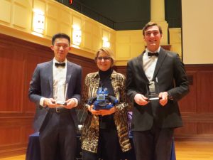 Three people posing for a photo with the two people on the outside are holding their trophies for the winning the Mayo business plane and the person in the middle is holding their invention.