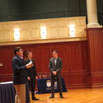 Three people standing in front of table presenting their business plan.